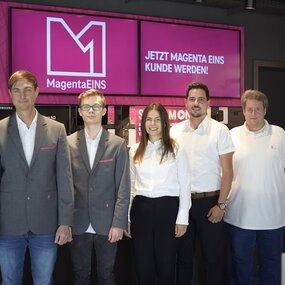 Fünf Telekom-Mitarbeiter stehen vor MagentaEINS-Werbung in einem modernen Shop.