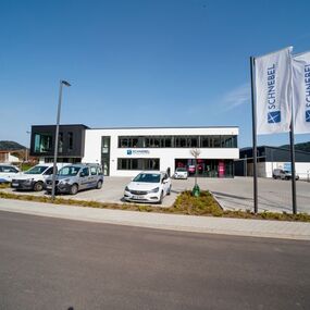 Modernes Firmengebäude mit Parkplätzen, Autos und Firmenflaggen von Schnebel und Telekom.